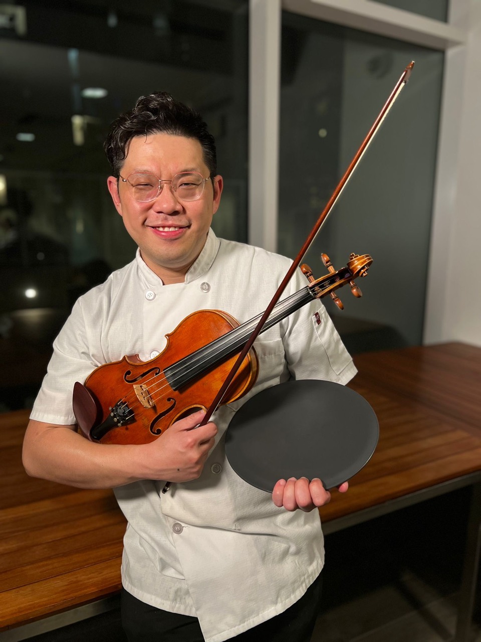 Abraham Wong in a chef coat holding a violin and a plate in Vancouver
